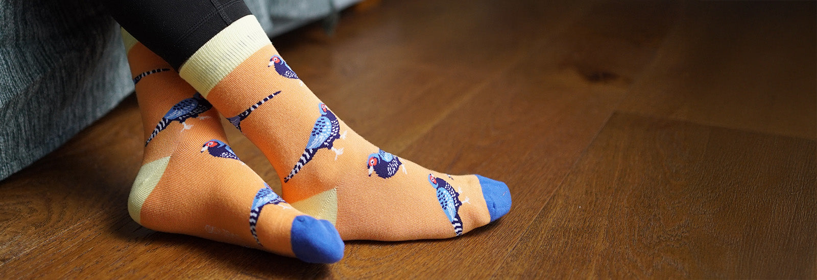 Person wearing orange socks with pheasant design on a wooden floor