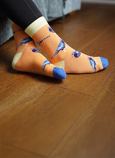 Person wearing orange socks with pheasant design on a wooden floor
