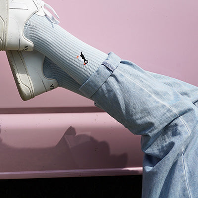 Person wearing light blue Puffins ribbed socks and white sneakers with a pink background