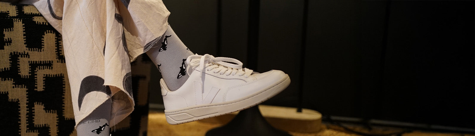 Person wearing white sneakers and small motif Orcas socks on a dark background