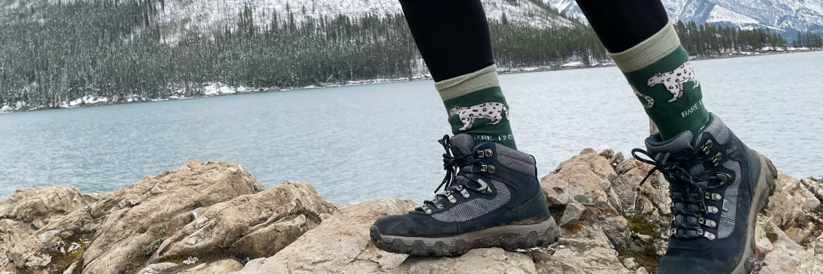 model wearing snow leopard bamboo socks on a rock with a snowy view