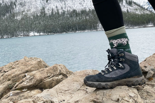 model wearing snow leopard bamboo socks on a rock with a snowy view