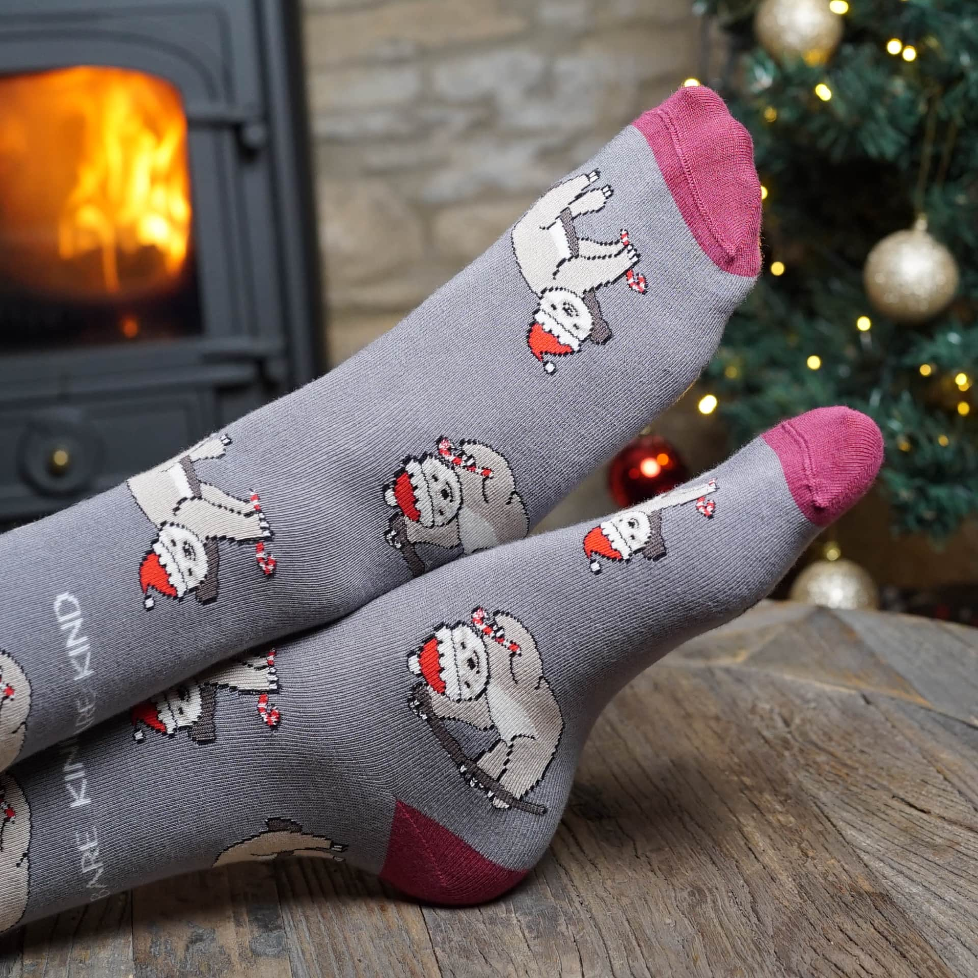 lifestyle image of model wearing grey sloth christmas bamboo socks in front of christmas tree and log fire