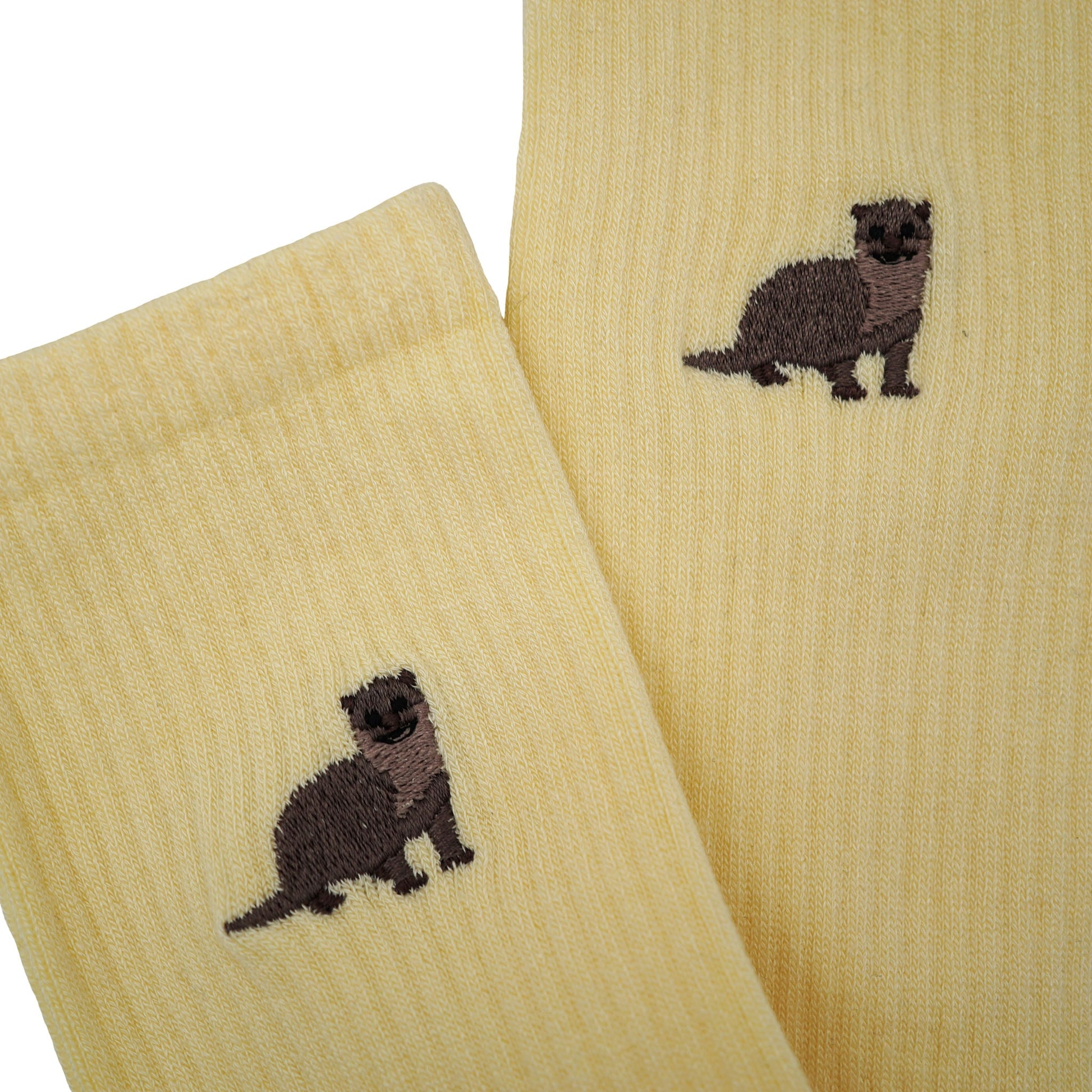 Close up to minimalist flat lay of pastel yellow ribbed bamboo socks with embroidered otter motif on the cuf