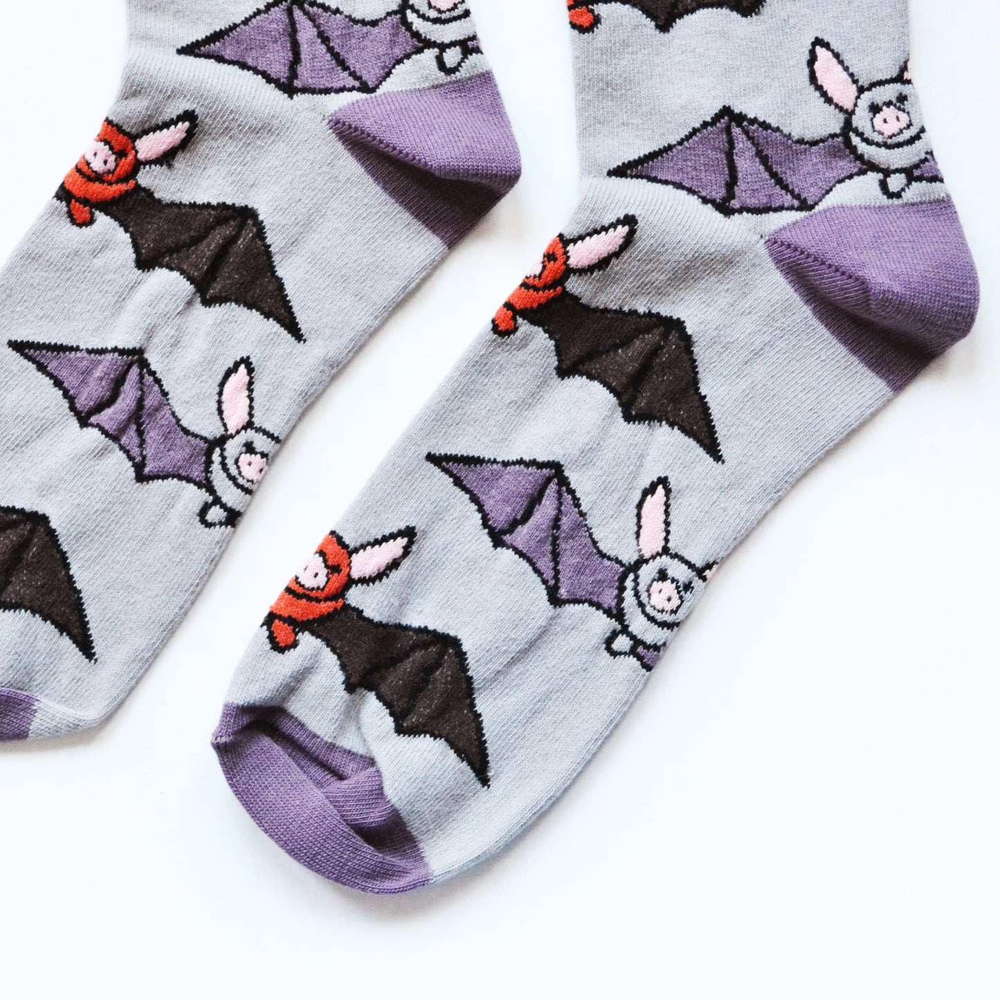 Flat lay of purple and grey bamboo socks with bats woven into the design. Image depicts a closeup of the toes