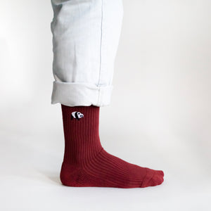 minimalist view of standing model wearing ruby red ribbed panda socks showcasing the embroidered panda motif on the cuff from the side