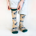 Model front view wearing cream and green bamboo cow socks as they pull the left cuff up