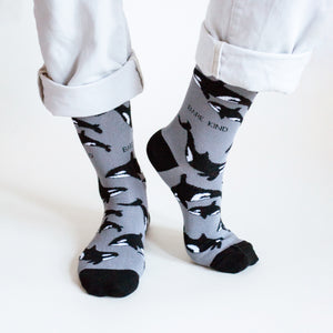 standing model wearing black and grey orca bamboo socks with the left heel up