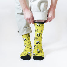model stands and pulls up the left cuff of black and yellow bamboo bee socks 