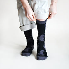 front view of model wearing black panther bamboo socks and pulling the left cuff up