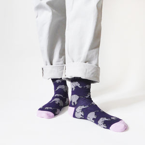 standing model wearing purple and pink elephant bamboo socks; the left foot is forward and angled to the side