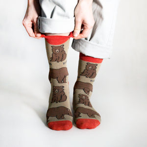 Model pulls up brown and red bamboo bear sock from the right cuff as they stand facing the viewer