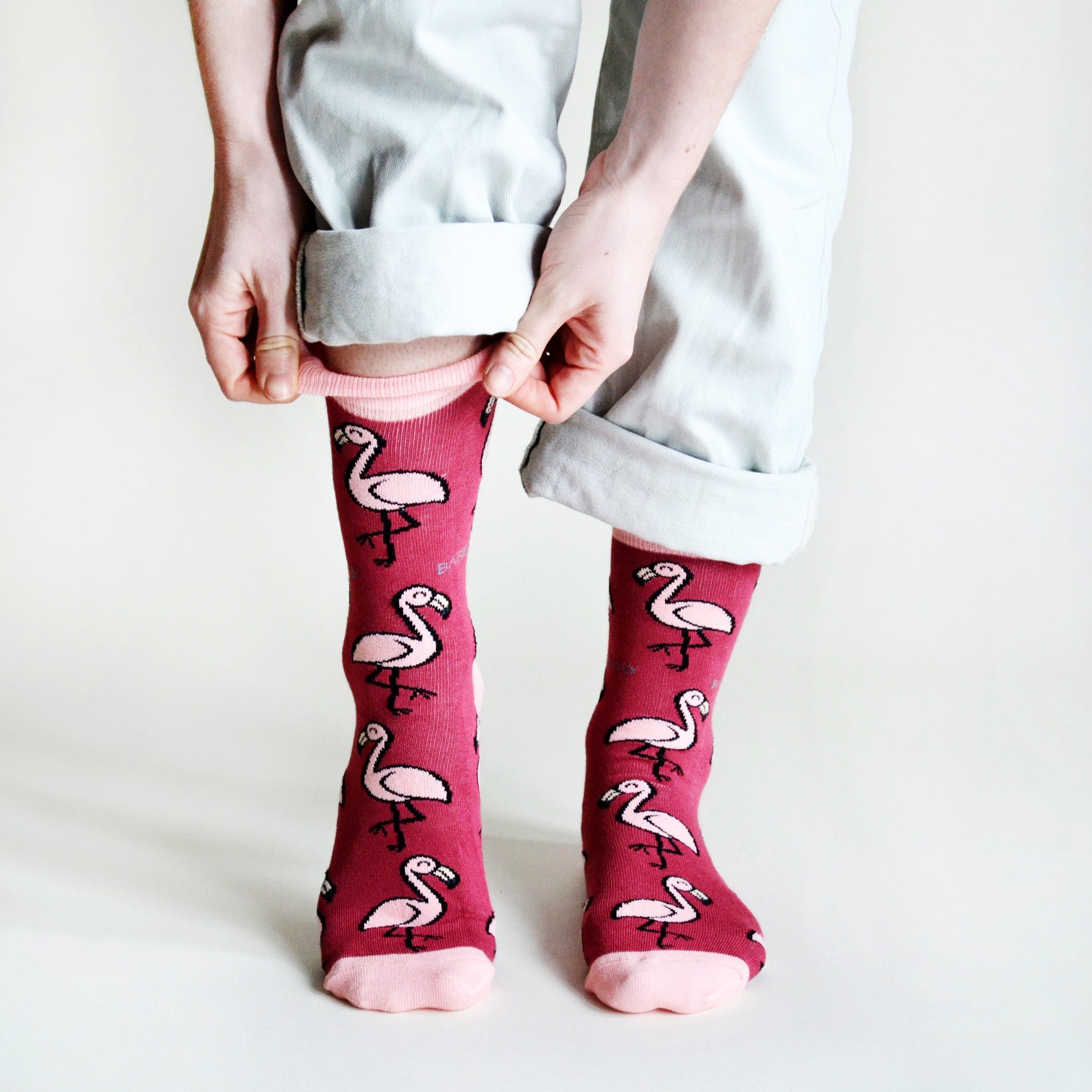 standing model wearing hot pink flamingo socks, pulling right cuff up, front view