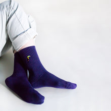 sitting model with ankles crossed wearing ribbed purple toucan socks