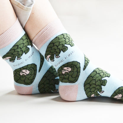 closeup side view of sitting model wearing pastel blue pangolin socks, showcasing the woven pangolin design