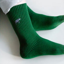 model lays with ankles crossed, wearing emerald green ribbed elephant socks depicting an embroidered elephant motif on the cuff