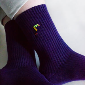 closeup of embroidered toucan motif on the cuff of ribbed purple bamboo socks