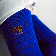 closeup of embroidered tiger motif as model sits with ankles crossed, birds eye view